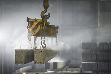 The crane moves a reinforced concrete product with holes.
Reinforced concrete pillars fixed with metal hooks and chains on the background of the plant